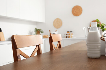 Wooden island table with bottle of milk and chairs in modern kitchen