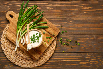Board and bowl of tasty sour cream with sliced green onion on wooden background