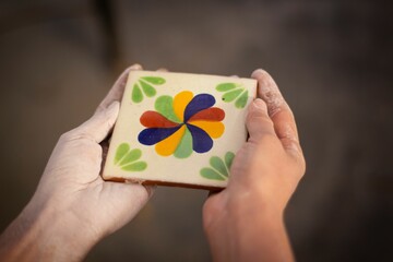 Closeup of dusty human hands holding beautiful square Mexican ceramic tile with floral patterns