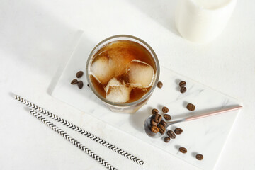 Glass of ice coffee with bottle of milk, beans and straws on white grunge background