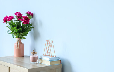 Vase with red peonies, candle and books on dresser near blue wall