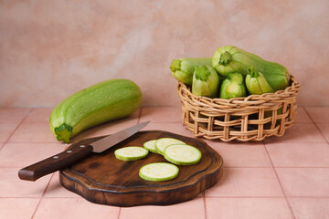 Wooden board and wicker basket with raw zucchini on table