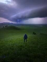 Vertical shot of a hiker on a grassy pasture looking at lightning in the distance
