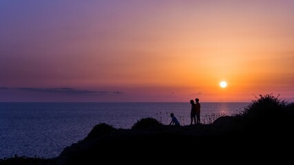 Silhouettes of children on the coast of a sea at a bright orange sunset