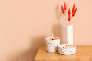 Holders with burning candles and lagurus on table near beige wall in room