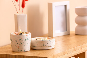 Holders with burning candles on table near beige wall in room, closeup