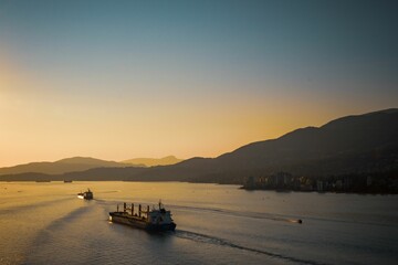 Aerial view of a ship sailing in a sea near a harbor against mountains at sunset
