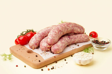 Board with raw fresh sausages, tomatoes and spices on beige background