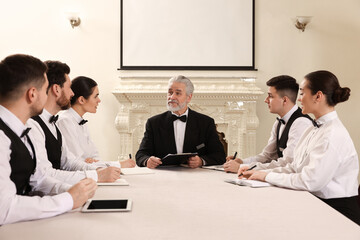 Senior man in formal suit teaching trainees indoors. Professional butler courses