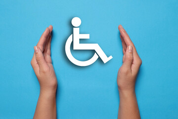 Disability inclusion. Woman protecting wheelchair symbol on light blue background, closeup