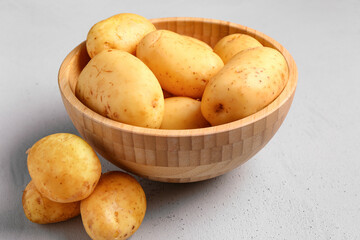 Wooden bowl with raw baby potatoes on grey background
