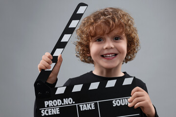 Smiling cute boy with clapperboard on grey background. Little actor - obrazy, fototapety, plakaty