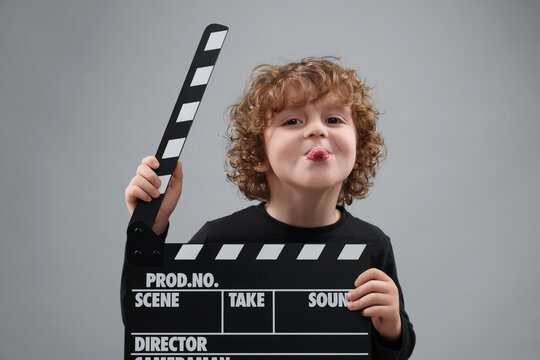 Happy cute boy with clapperboard on grey background. Little actor