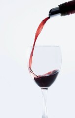 Red wine bottle pouring on a wine glass isolated on white background, vertical shot