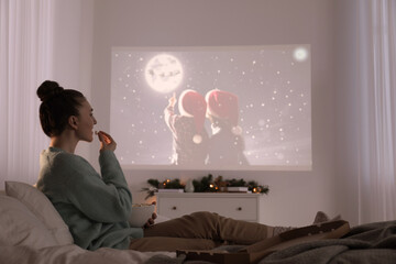 Woman with popcorn watching Christmas movie via video projector at home - obrazy, fototapety, plakaty