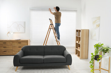 Man on wooden folding ladder installing blinds at home, back view