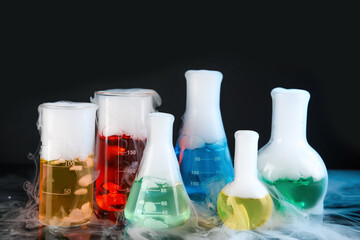 Laboratory glassware with colorful liquids and steam on black background. Chemical reaction