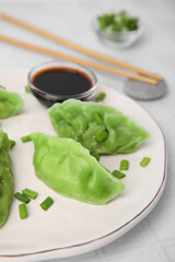 Delicious green dumplings (gyozas) and soy sauce on white tiled table, closeup