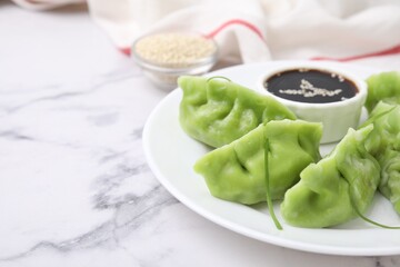 Delicious green dumplings (gyozas) and soy sauce on white marble table, closeup. Space for text