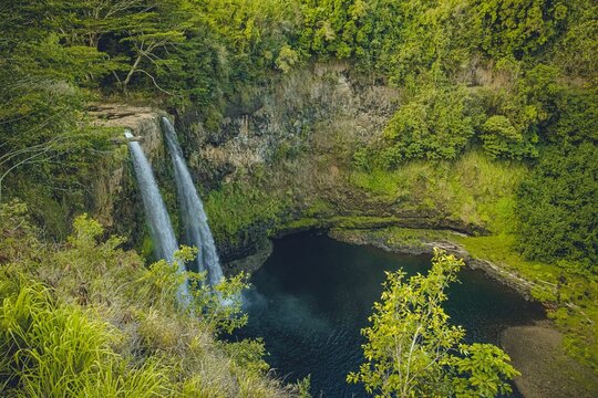 Drone shot of waterfalls flowing to a lake surrounded by lush greenery