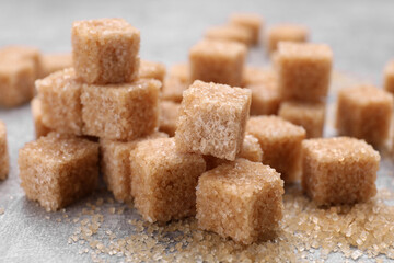 Many brown sugar cubes on grey table, closeup