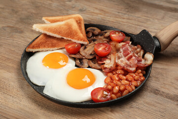 Serving pan with fried eggs, mushrooms, beans, bacon, tomatoes and toasted bread on wooden table, closeup. Traditional English breakfast