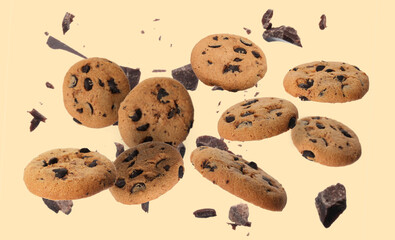 Delicious chocolate chip cookies and pieces of chocolate falling on beige background