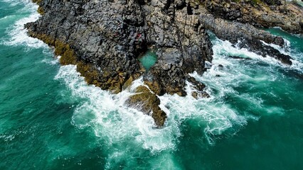 Aerial view of sea waves breaking rocky and greenery beach