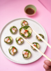 Masculine hand hold chopsticks with maki on pink background