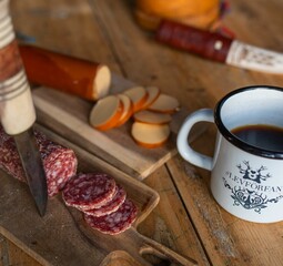 Closeup of a breakfast on the table with hot coffee, salami and cheese on the blurred background