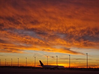 Beautiful scenery of a plane landing at sunset with a vibrant cloudy orange sky in the background