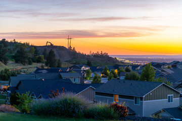 An empty heavy equipment excavator machine vehicle sits atop a hill of excavated dirt at sunset overlooking the lights of downtown Spokane, Washington USA.