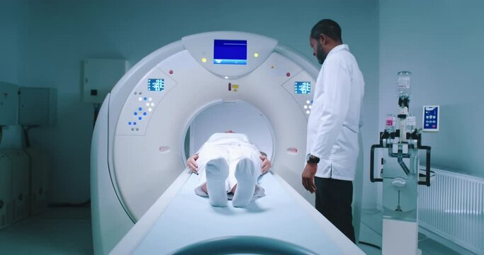 Patient after tomography procedure. Multicultural doctor finishes magnetic resonance imaging. Patient is lying at CT scanner bed and moving out of MRI capsule. Well-equipped tomography room.