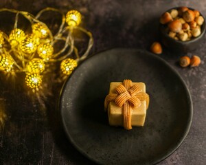 Hazelnut praline in black plate and garland lights next to it on the table with small bowl