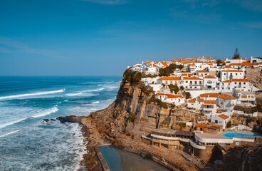 Aerial shot of white buildings with red roofs on a cliff by a sea in Azenhas do Mar, Portugal