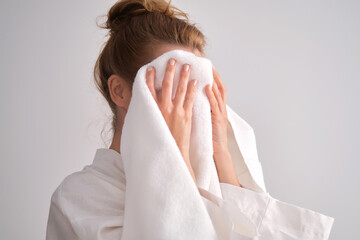 The girl wipes her face with a terry towel.