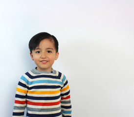 beautiful child, 5 year-old kid, little smile showing teeth, serious expression, beige sweater with color stripes, arms at sides, latin boy, White background,  light skin, pink cheeks, 