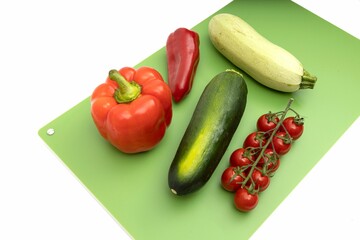 Vegetables on green professional chopping board on white background