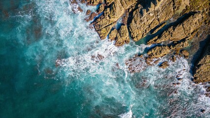 Top aerial view of blue waves crashing on the rocky coastline, summer seascape