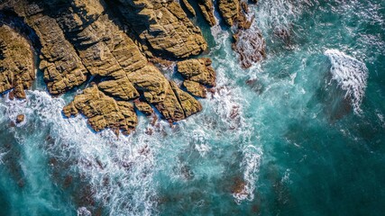 Top aerial view of blue waves crashing on the rocky coastline, summer seascape