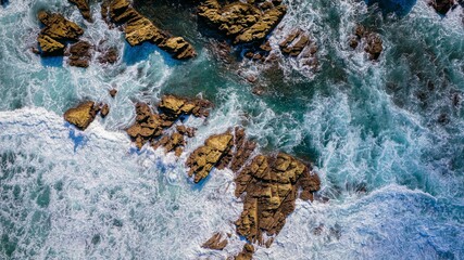 Top aerial view of blue waves crashing on the rocky coastline, summer seascape