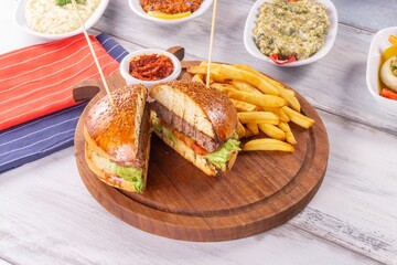 a burger on a wooden plate with french fries and dipping sauces