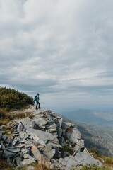 Vertical shot of a hiker at a distance standing on the top of rocky hill against cloudy sky