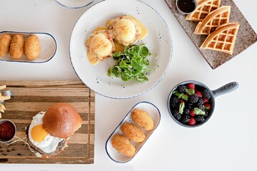 Top view of a table with gourmet breakfast dishes like waffles, egg benedict, and berries