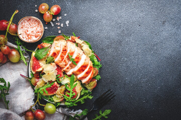 Gourmet salad with fresh figs, grilled chicken, parmesan cheese, grape, arugula, swiss chard with wine vinegar dressing. Black kitchen table background, top view