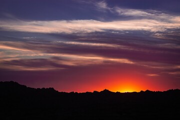 Fototapeta premium Glowing crimson sky at dusk with a majestic mountain range in the background.
