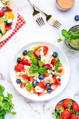 Fresh fruit and berry salad with cottage cheese, strawberries, blueberries, kiwis, oranges and mint leaves with honey dressing, marble table background, top view