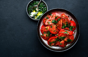 Simple vegan tomato salad with parsley, garlic, jalapeno and olive oil dressing, black table background, top view