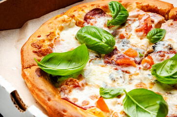Hot pizza in box with spicy salami sausage, mozzarella cheese, tomato sauce and green basil, just delivered, black table background, top view