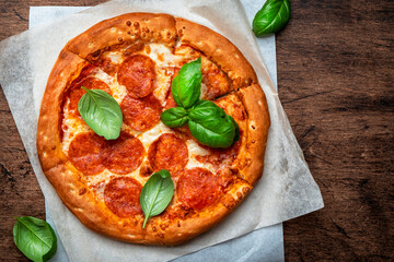 Hot pepperoni pizza with spicy salami sausage, mozzarella cheese, tomato sauce and green basil, white table background, top view